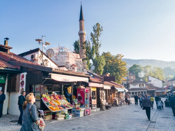 Baščaršija market street with fruit stalls and a mosque minaret behind