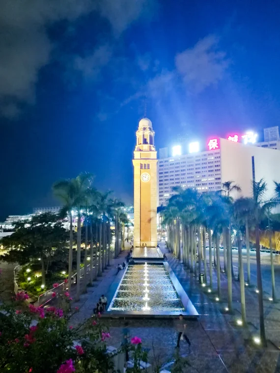 Tsim Sha Tsui Clock Tower in Hong Kong illuminated at night with palm trees