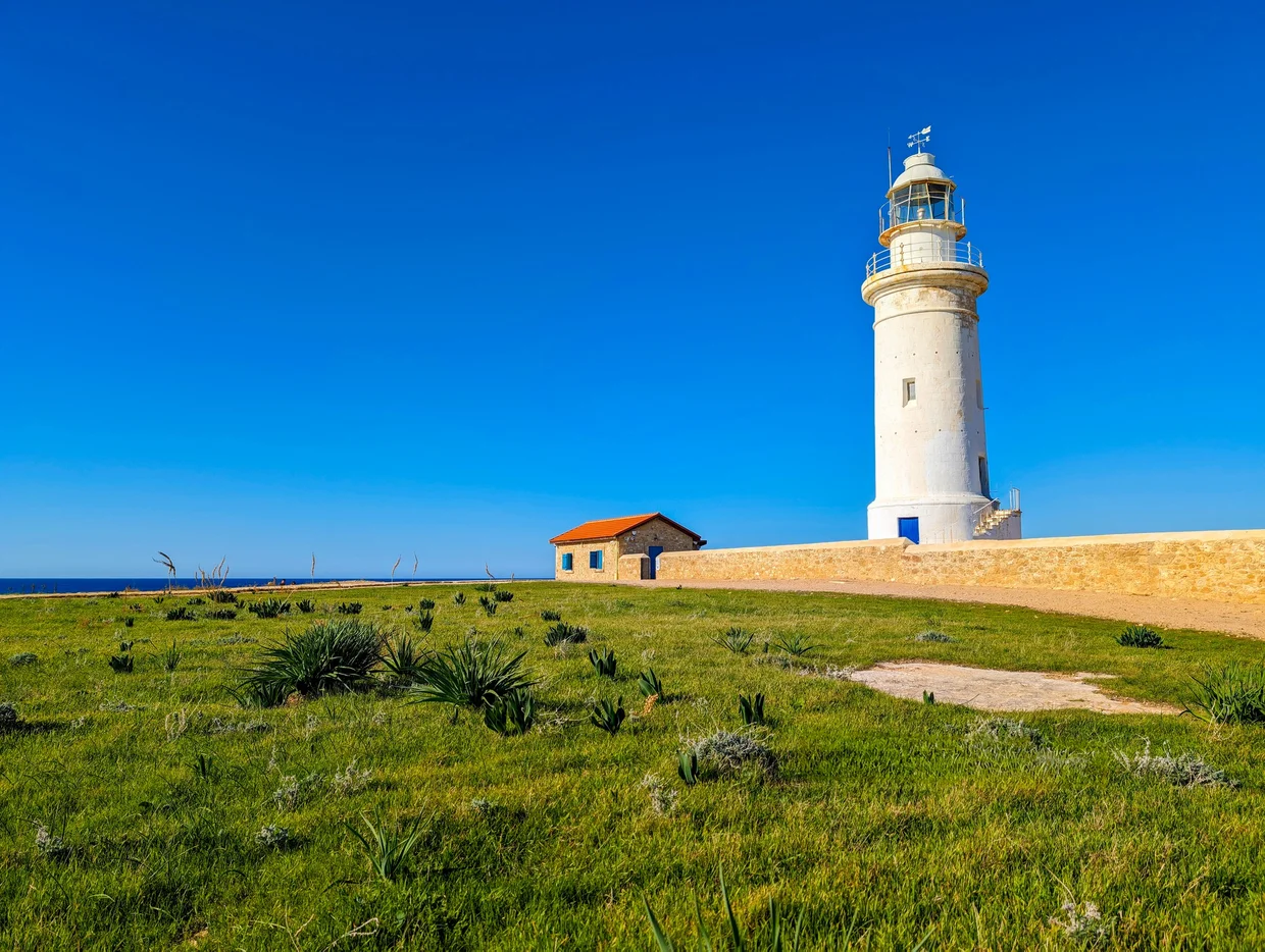 Paphos Lighthouse standing white against blue sky on a green hillside