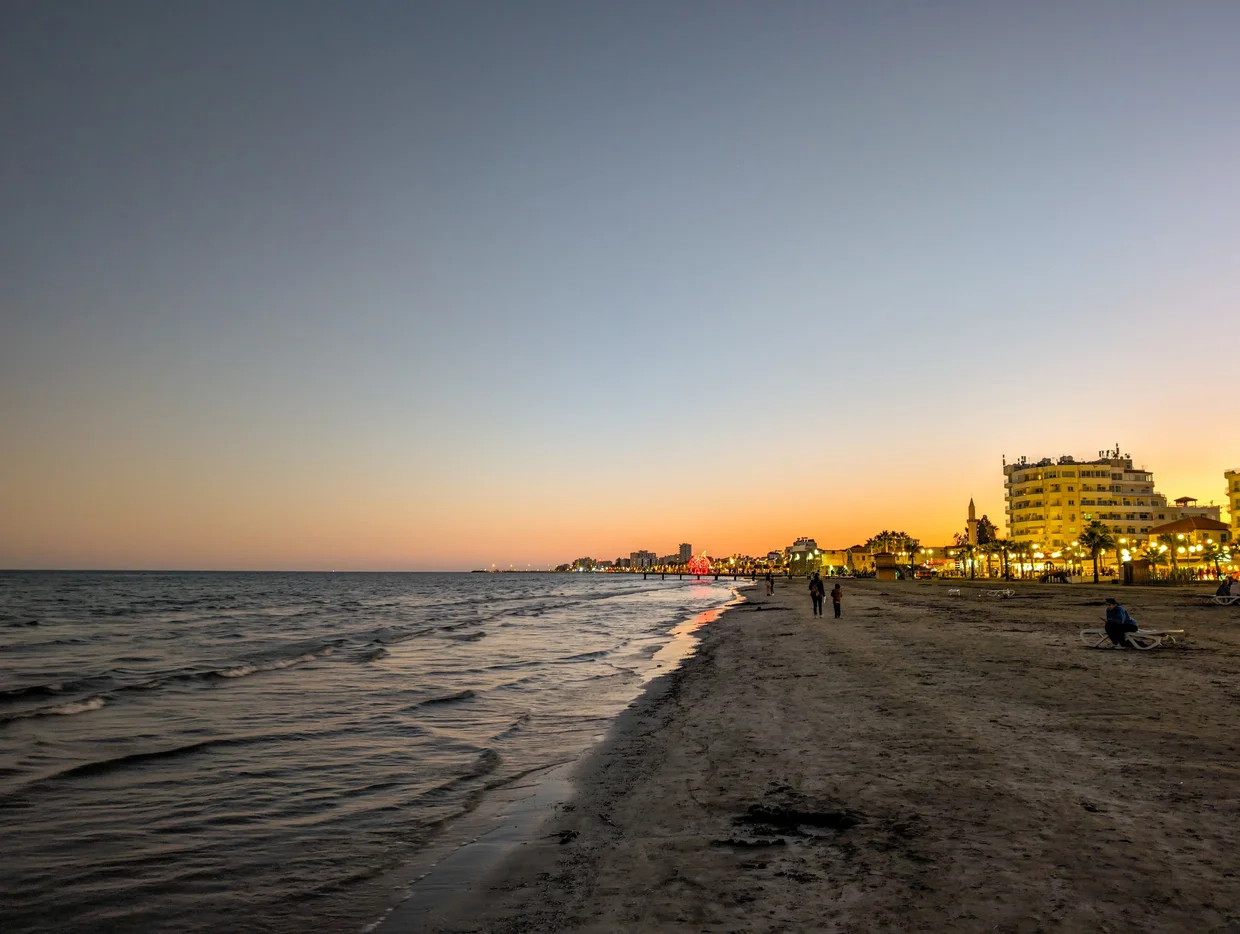 Larnaca beach at dusk with beachfront hotels lit up and people on the shore