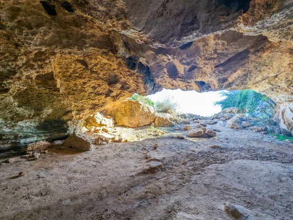 Looking out from inside a large cave toward bright daylight