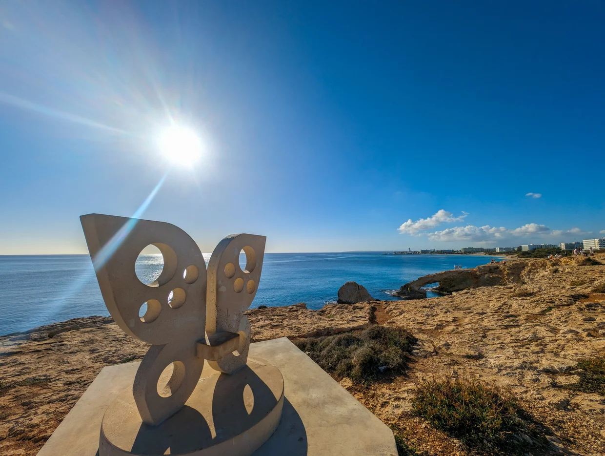 Modern sculpture on a coastal clifftop with sun flare and sea behind