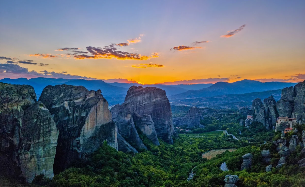 Sunset over the sandstone rock pillars of Meteora with distant mountains