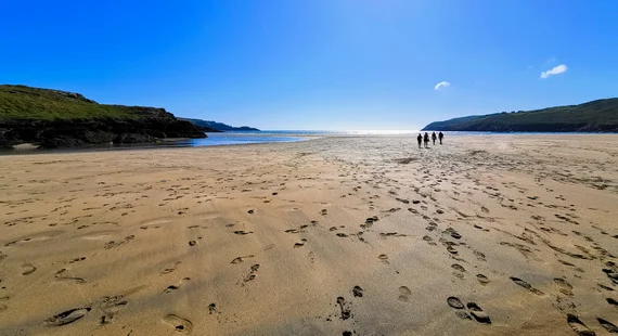 Footprints on a vast sandy beach at low tide, walkers in the distance