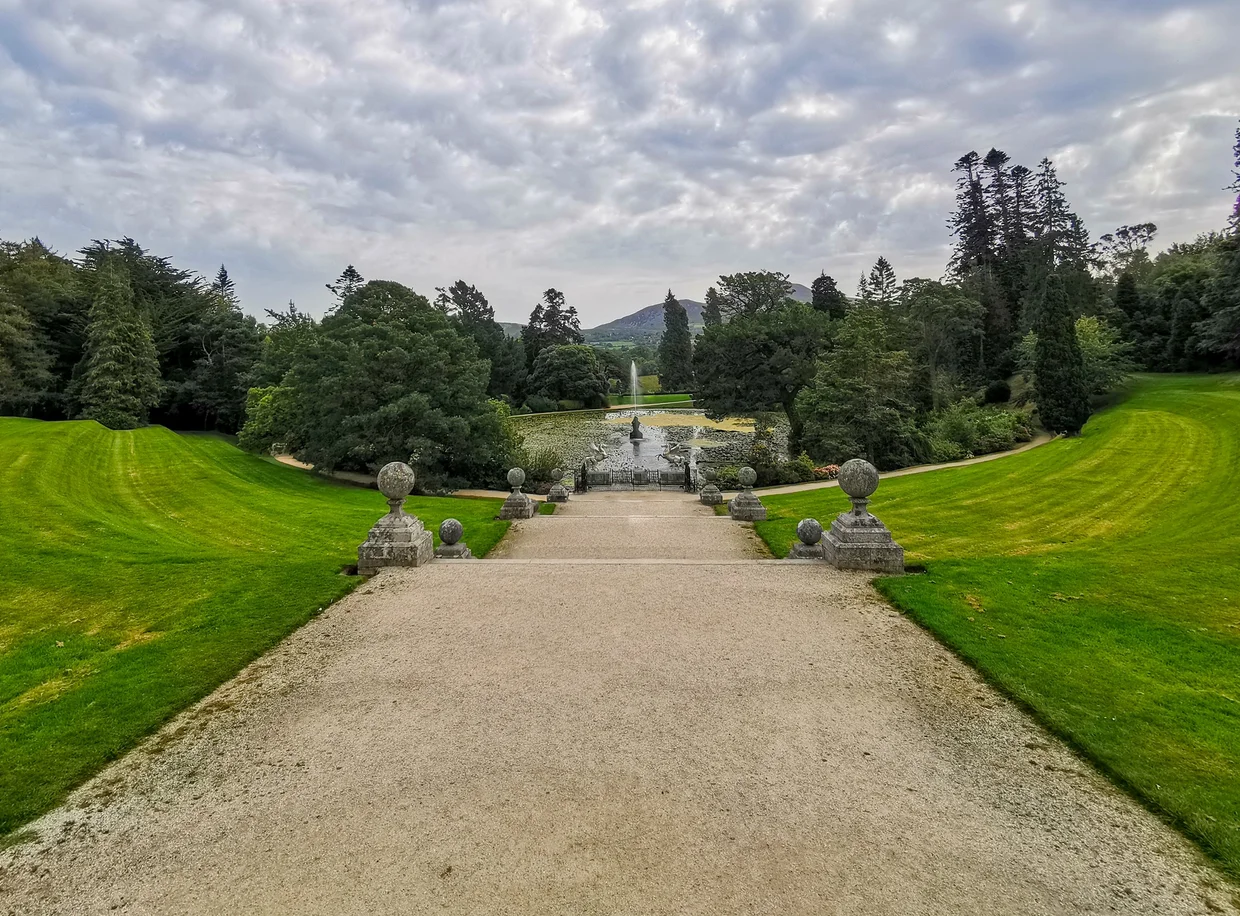 Grand stone pathway leading down through terraced gardens toward a distant fountain and mountain