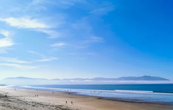 Wide sandy beach stretching to the horizon with hazy blue mountains beyond