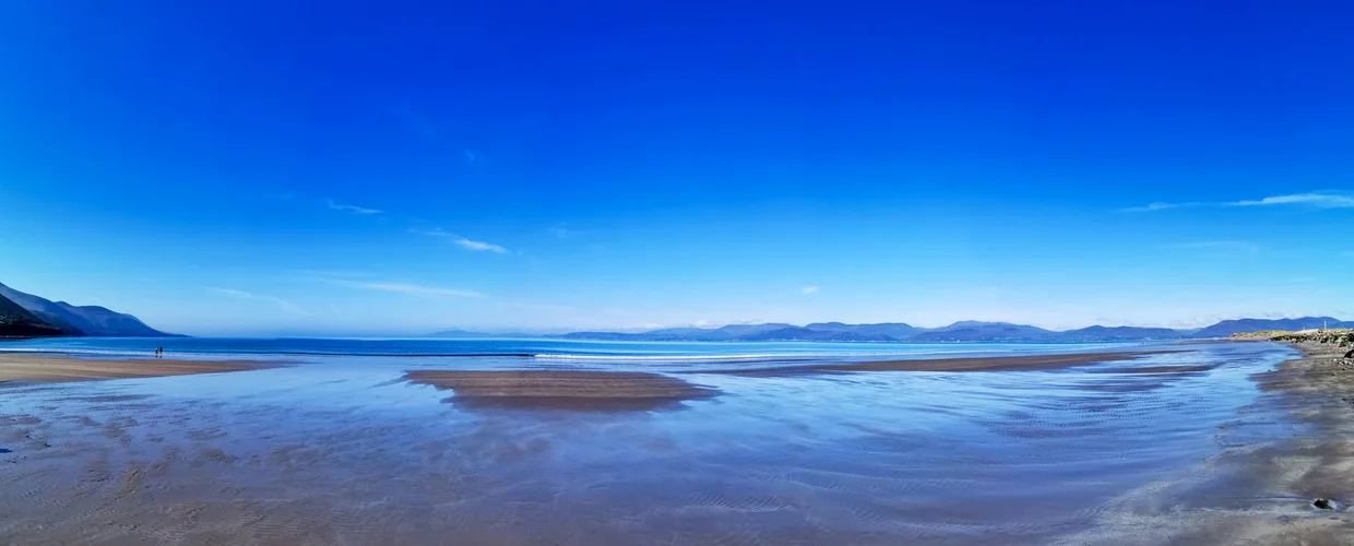 Vast beach at low tide, sky reflected in the wet sand, mountains on the horizon