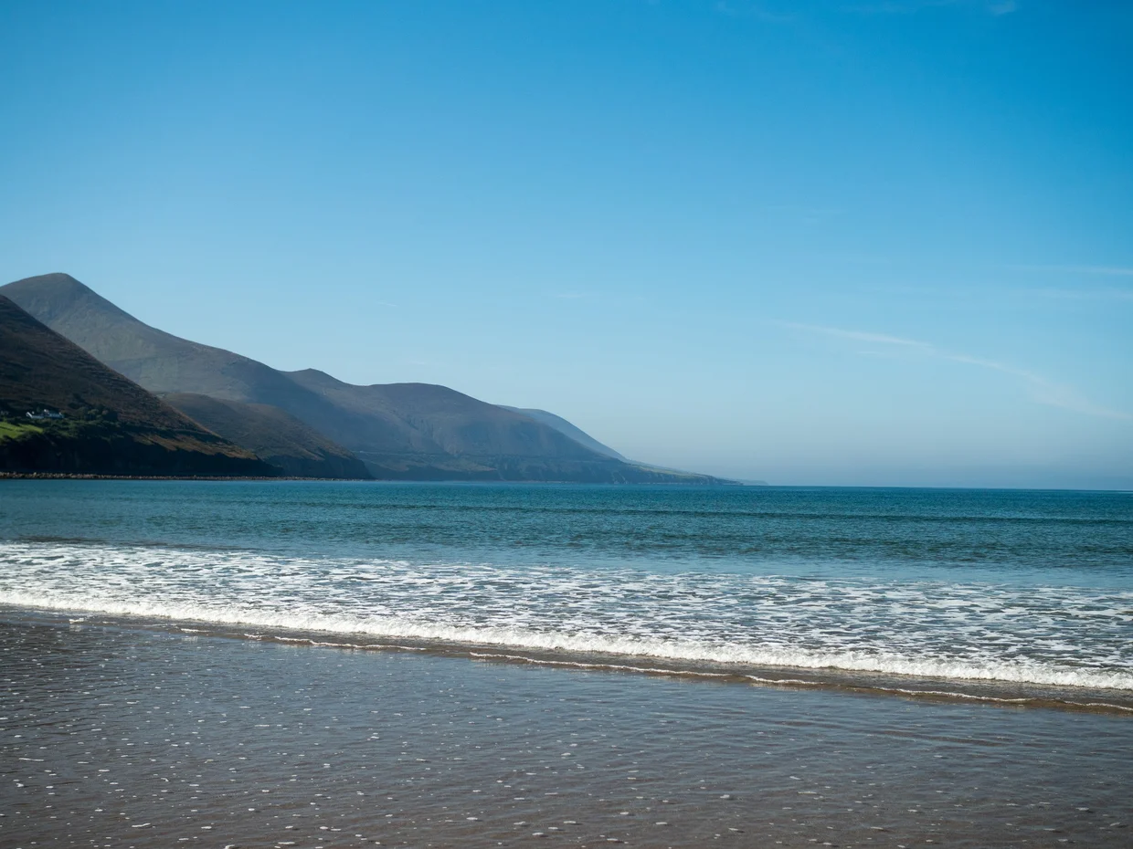Gentle waves washing onto a sandy beach with a misty mountain ridge rising behind