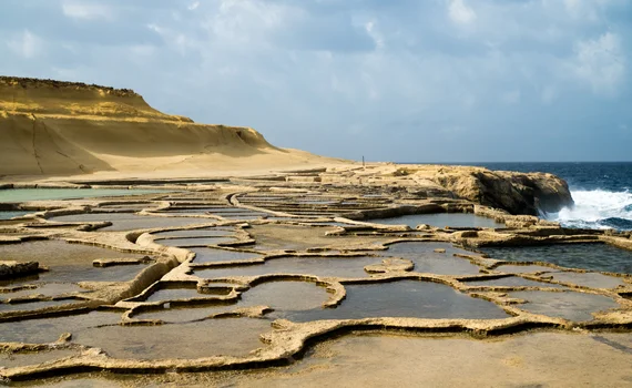 Wide view of salt pans with dramatic sandstone cliff in background