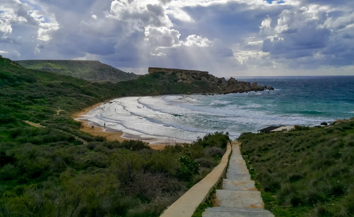 Steps leading down to a sandy bay with dramatic cloudy sky