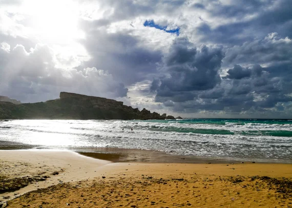 Sandy beach at water level with moody backlit clouds