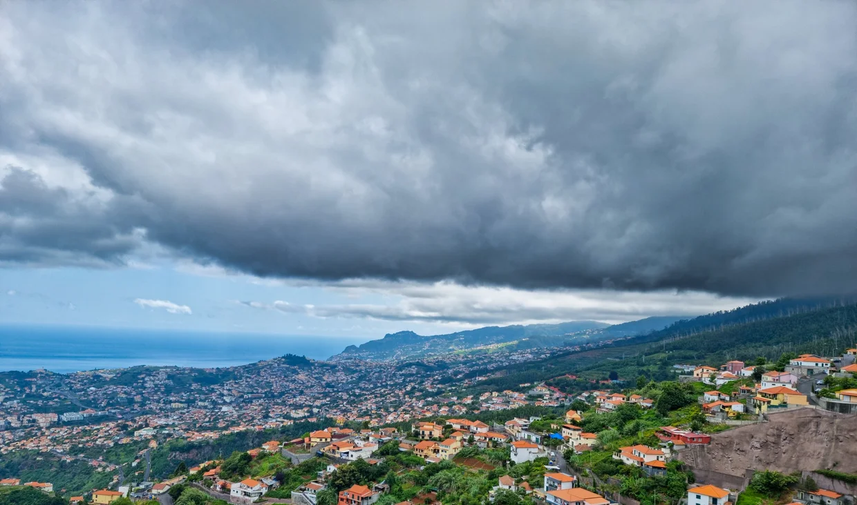 Funchal from above, orange rooftops spreading toward the coast under dramatic clouds