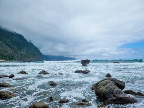 Rocky volcanic beach with waves and misty green mountains