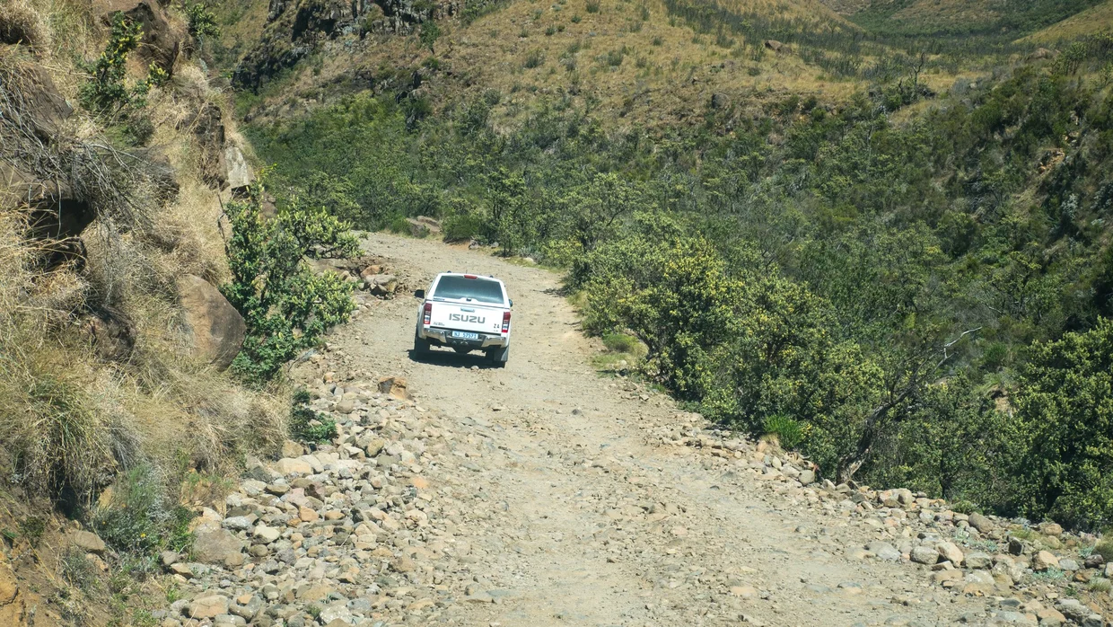 A white pickup truck navigating the rocky gravel road of the Sani Pass