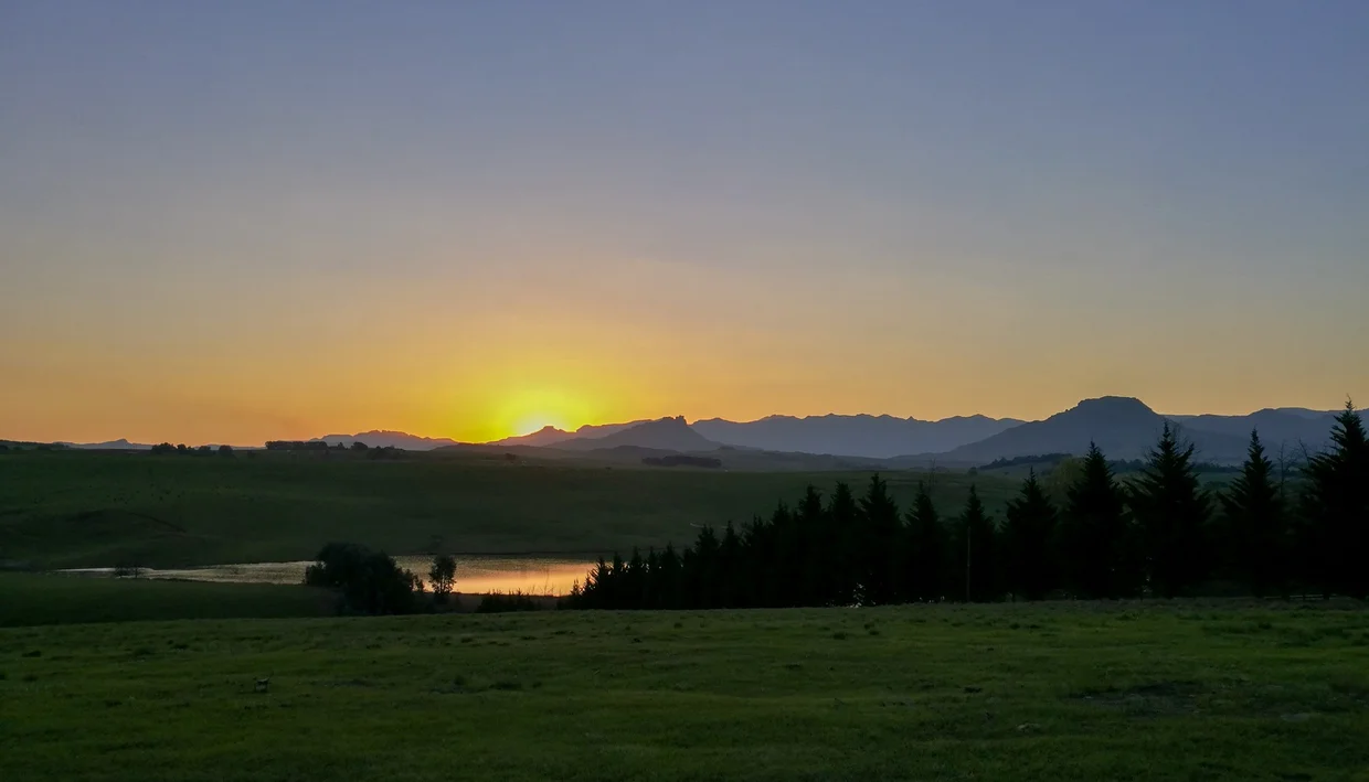 Sunset over green fields near Himeville with the Drakensberg mountains on the horizon