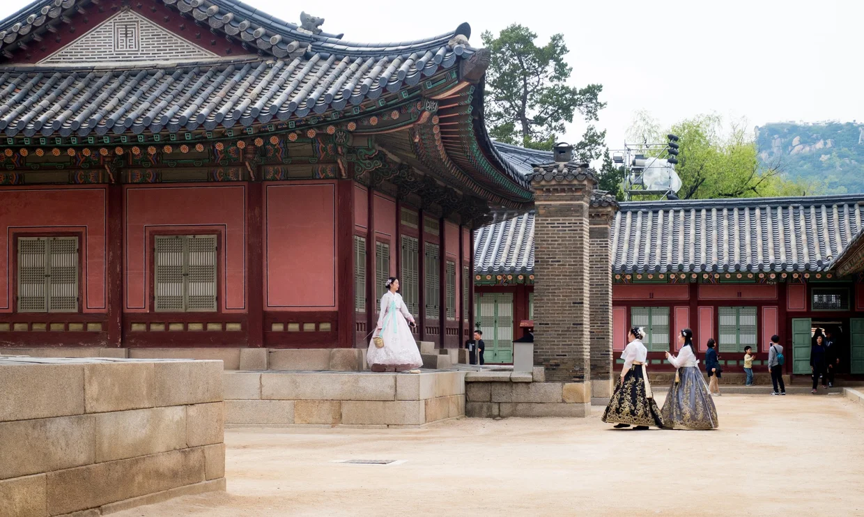 Visitors in hanbok posing at a red palace courtyard