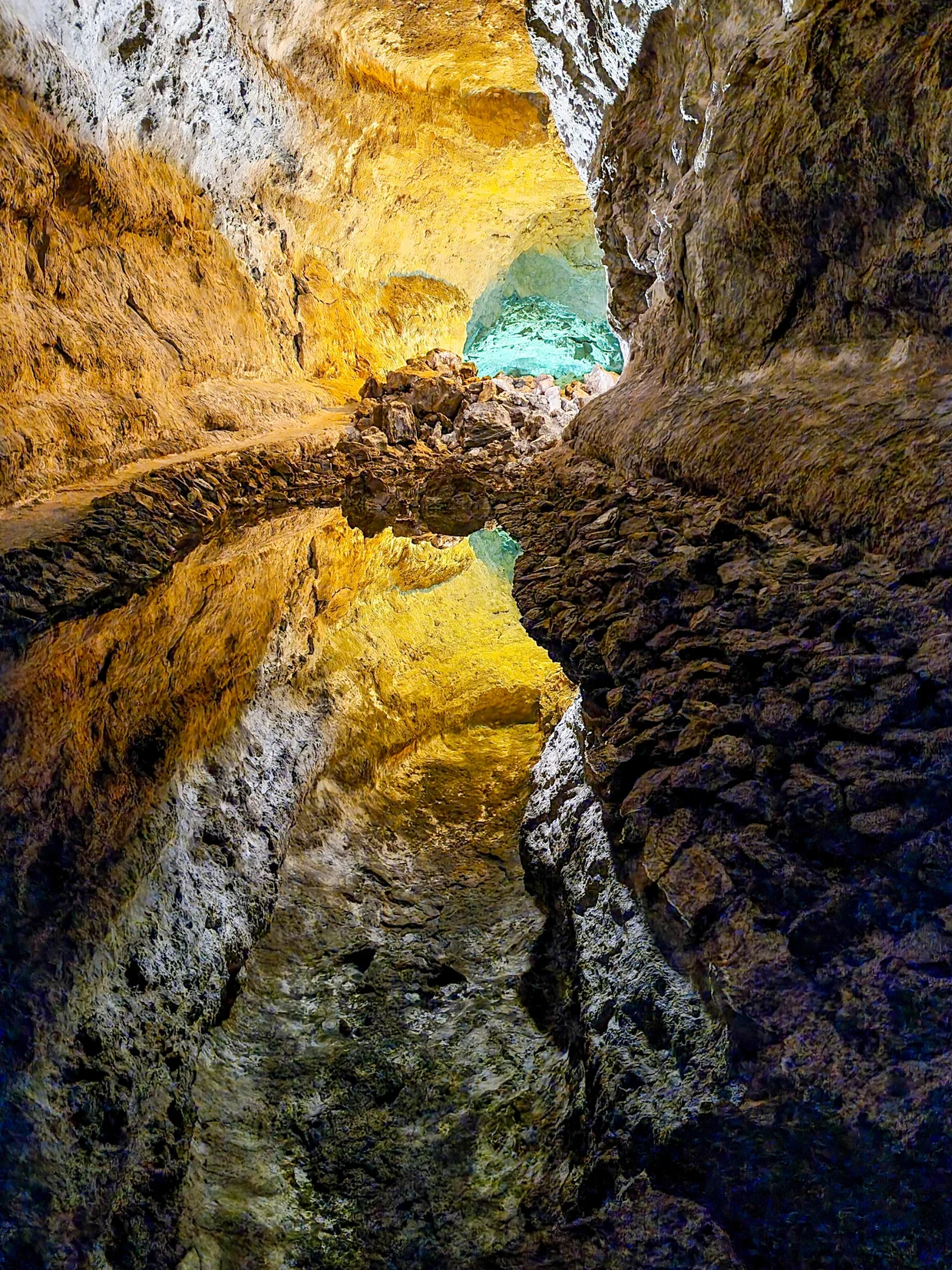 Underground lava tube with turquoise water pool and golden rock reflections