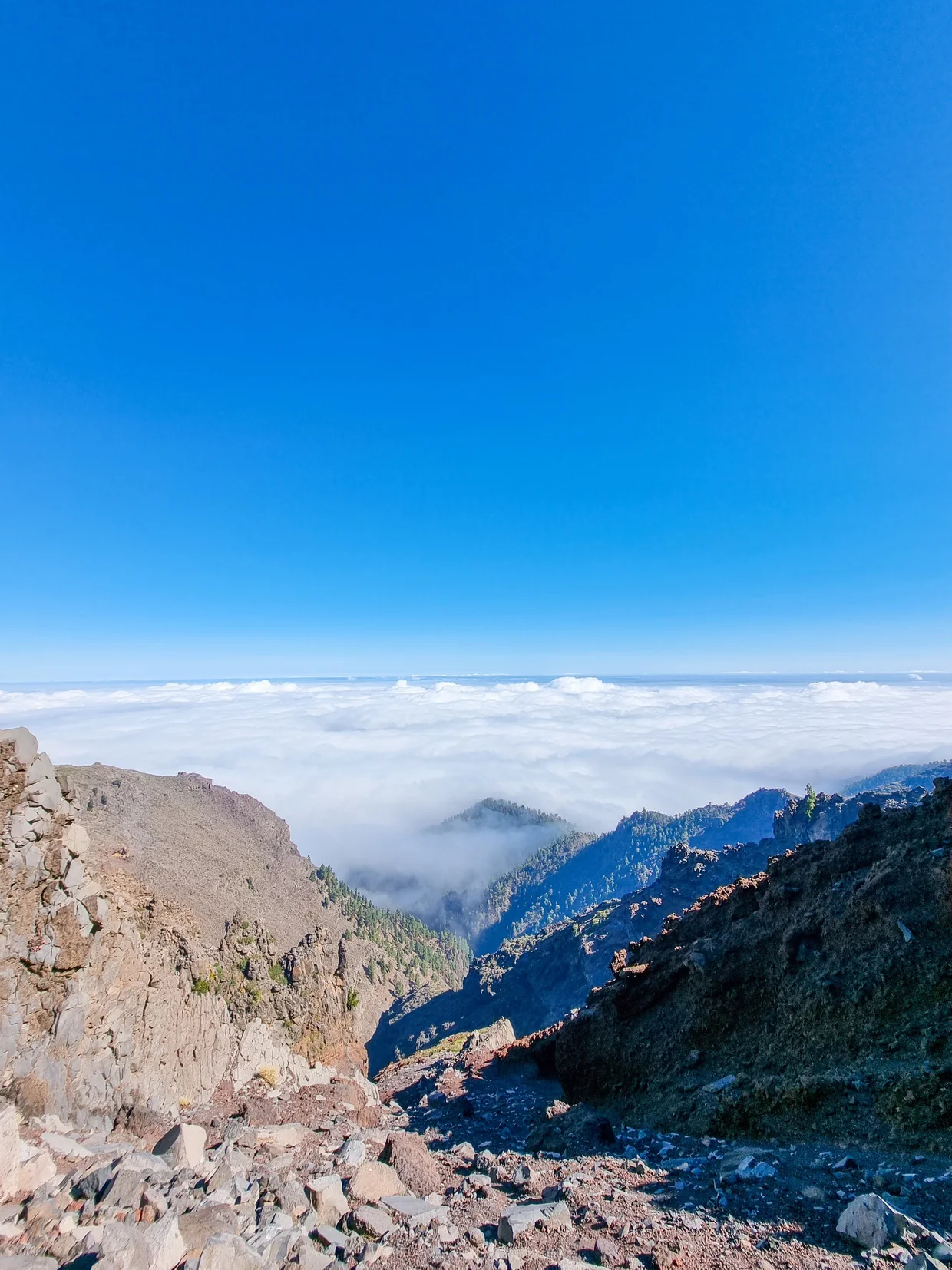 Summit view looking down into deep caldera with clouds filling valley and mountain ridges