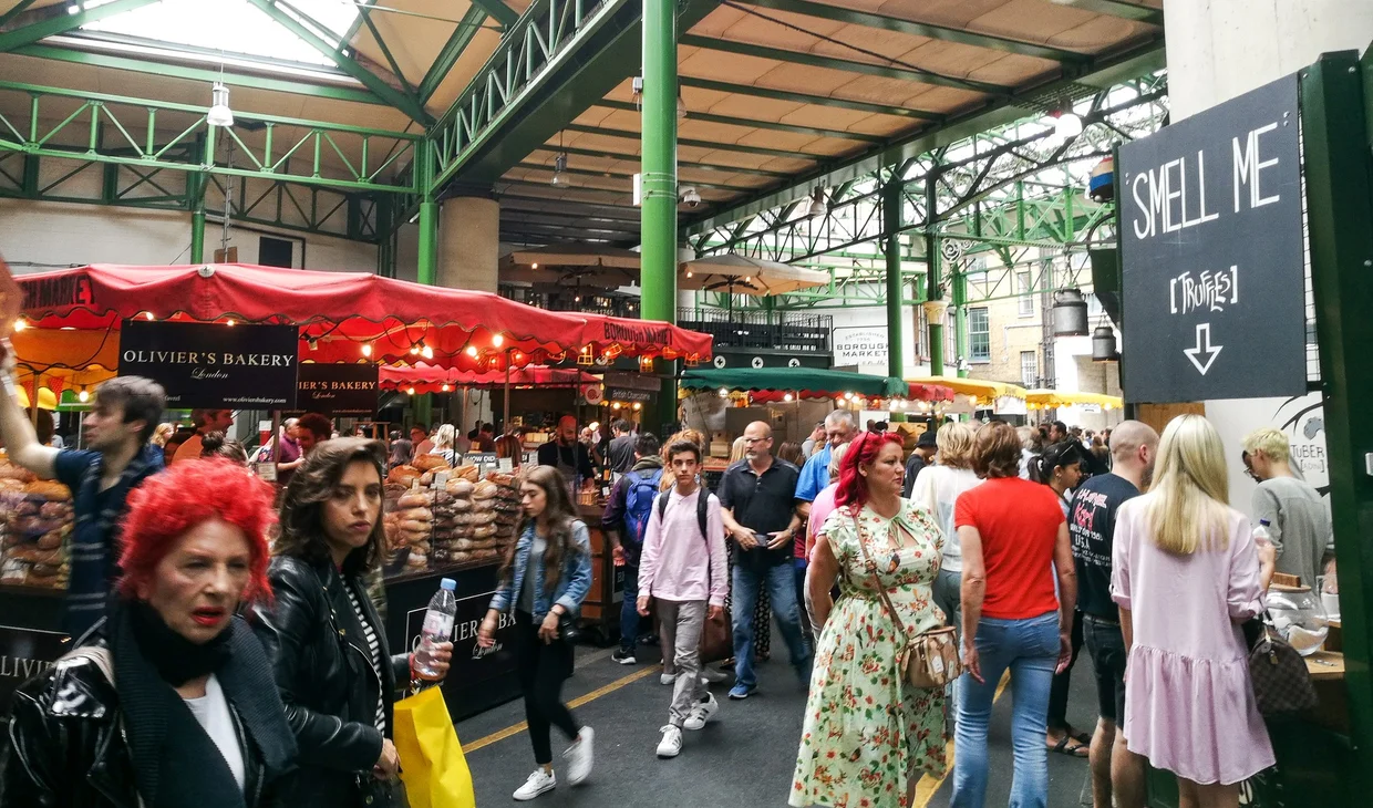 Inside Borough Market, crowds browsing stalls, bakery visible under green ironwork