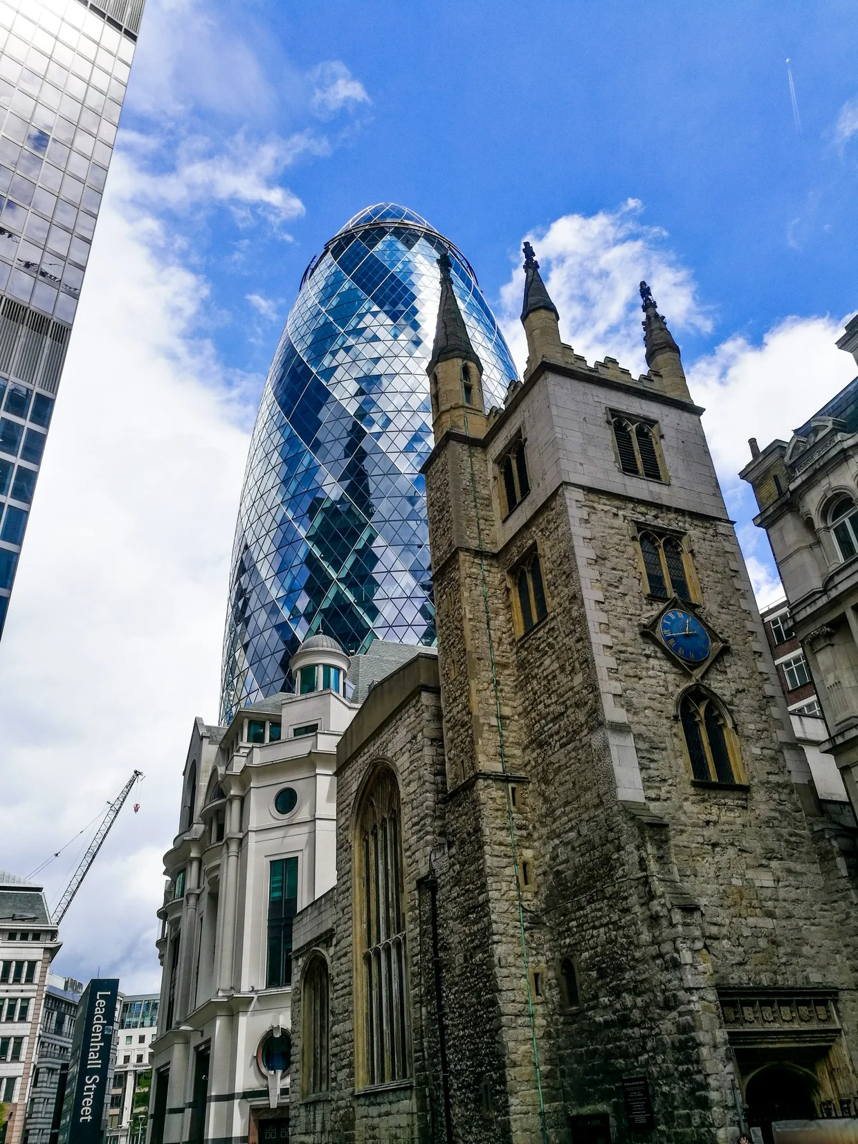 The Gherkin rising behind the stone tower of St Andrew Undershaft on Leadenhall Street
