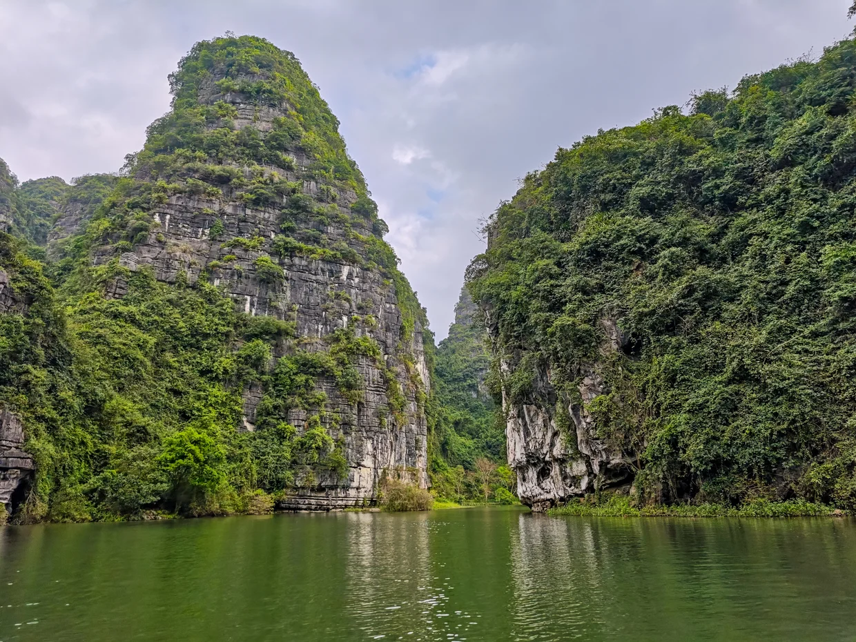 Narrow water channel between steep limestone cliffs at Trang An