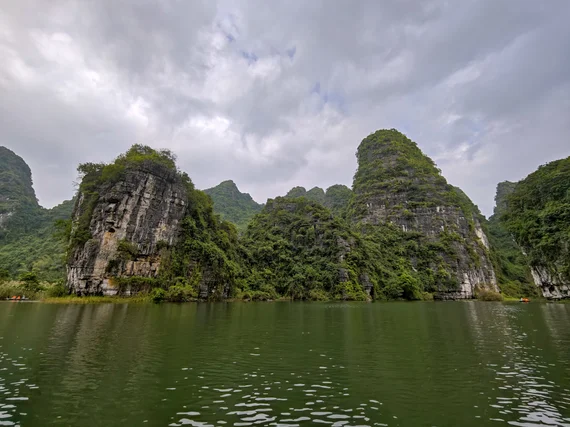 Rocky karst outcrop and forested cliffs reflected in the river at Trang An