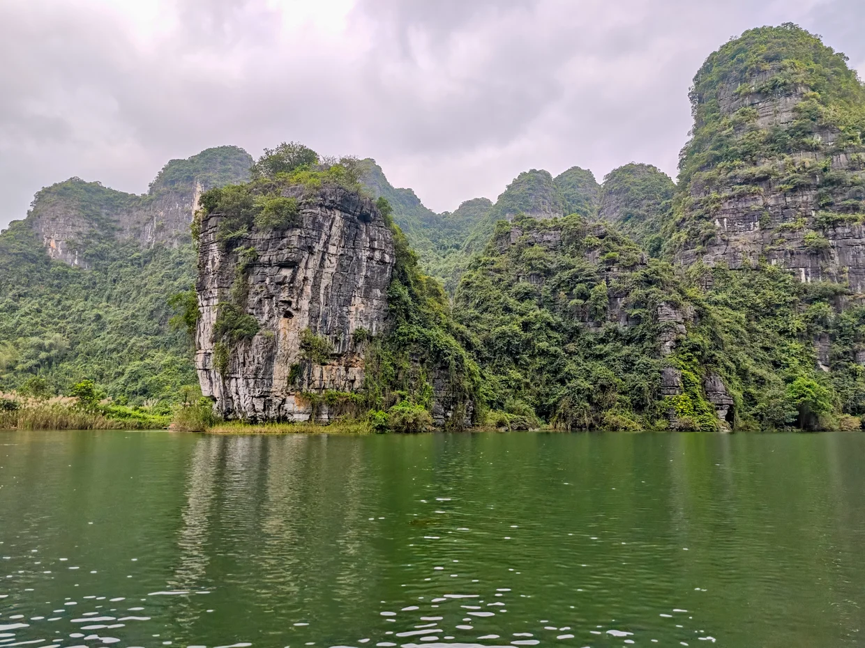 Wide view of green karst towers rising from calm water in Trang An